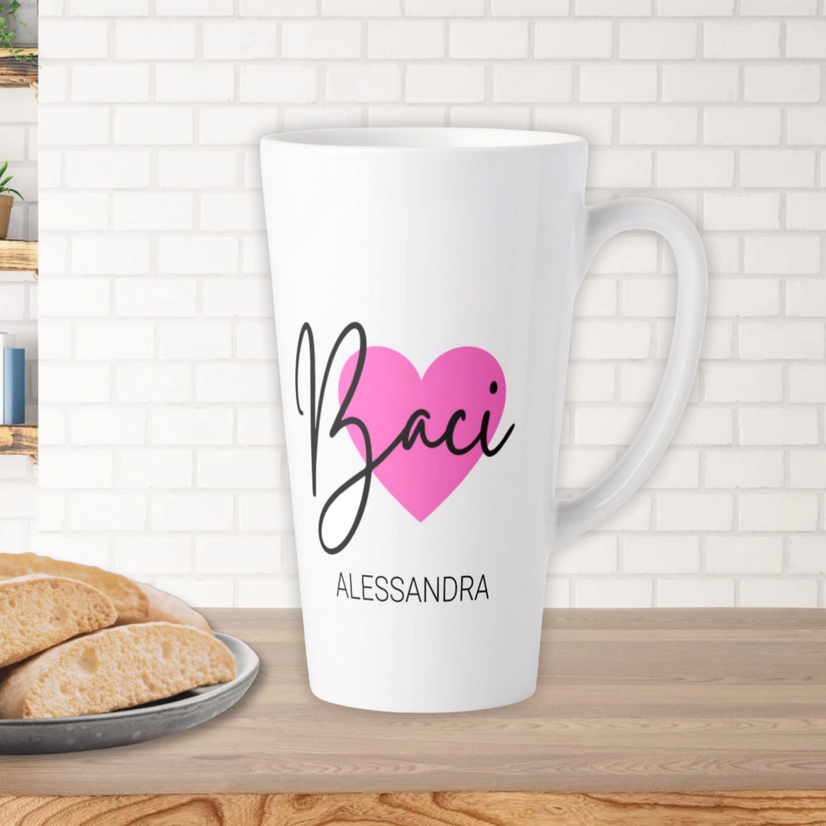 White latte mug with 'Baci' personalized design on a wooden counter with biscotti.