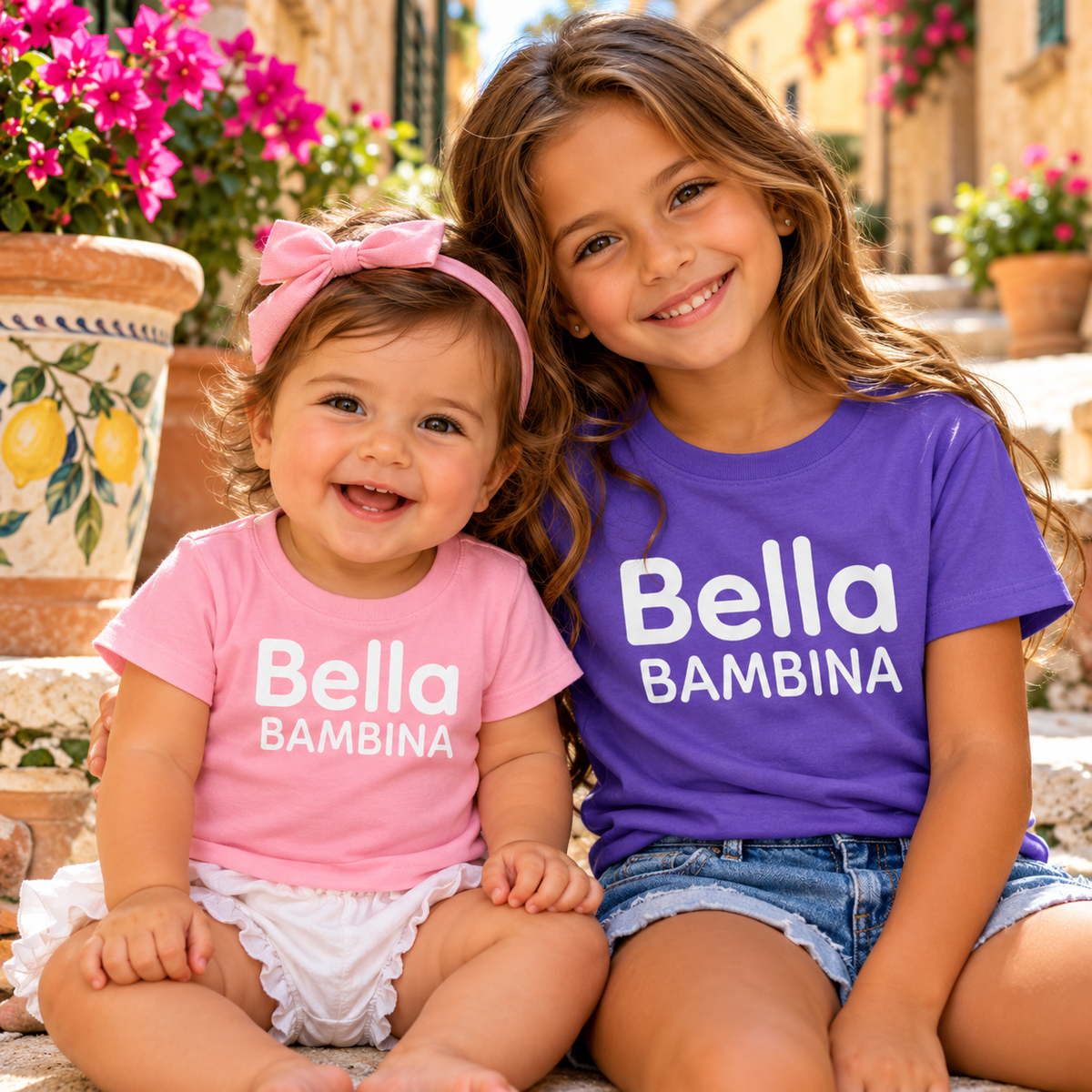 Two sisters wearing matching Bella Bambina Italian girls' T-shirts in pink and purple. Cute Italian heritage outfits for baby and kids.