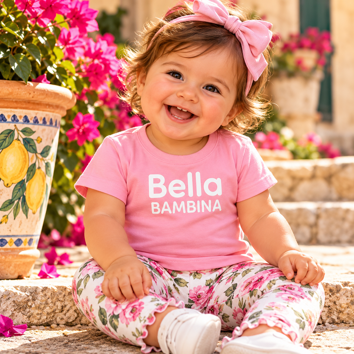 Smiling baby girl in pink Bella Bambina Italian heritage T-shirt, floral leggings and matching bow.