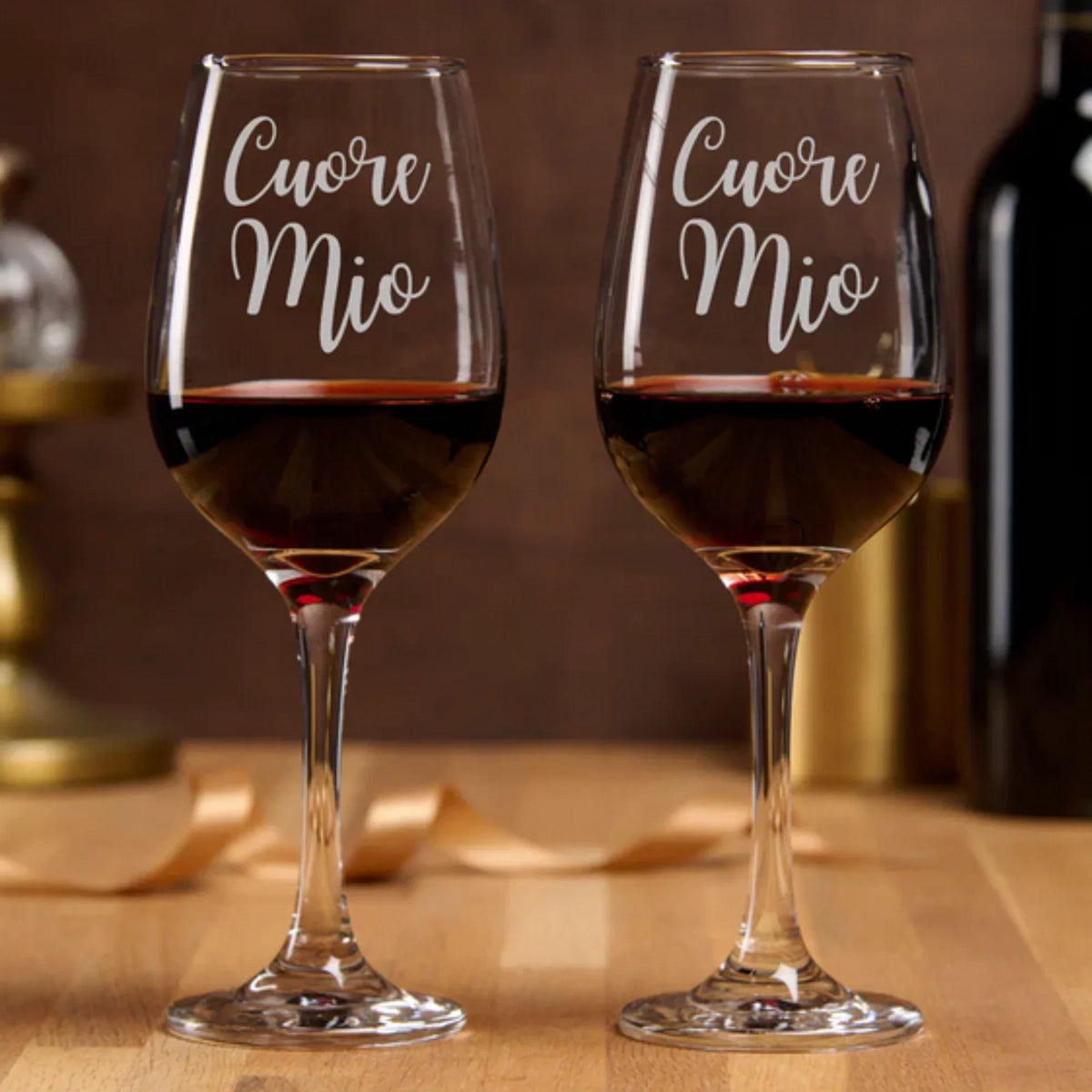 Two wine glasses with 'Cuore Mio' inscription filled with red wine on a wooden surface for Valentine's Day, wedding or anniversary gift.