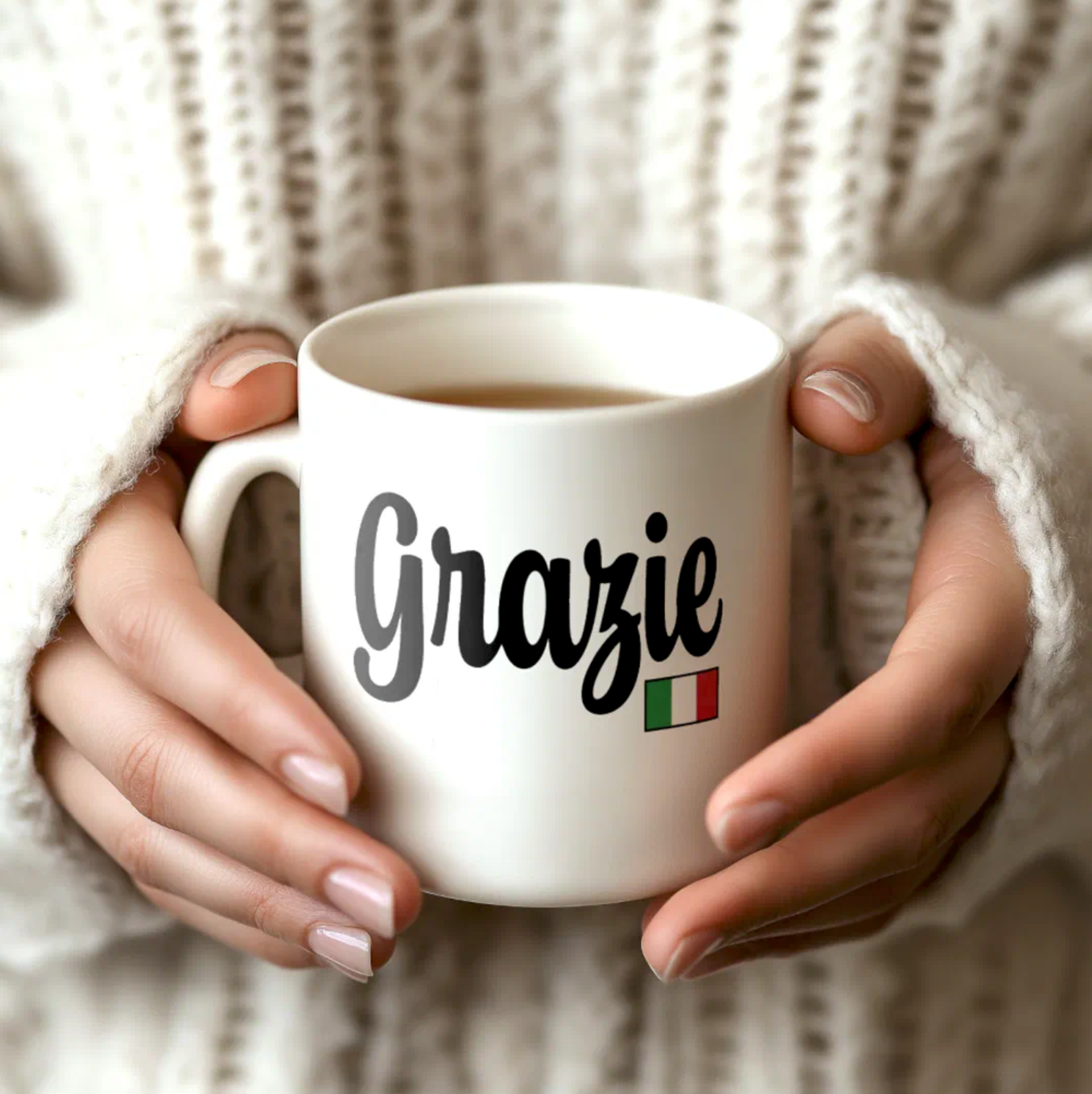 White mug with 'Grazie' and Italian flag held by hands against a textured beige background