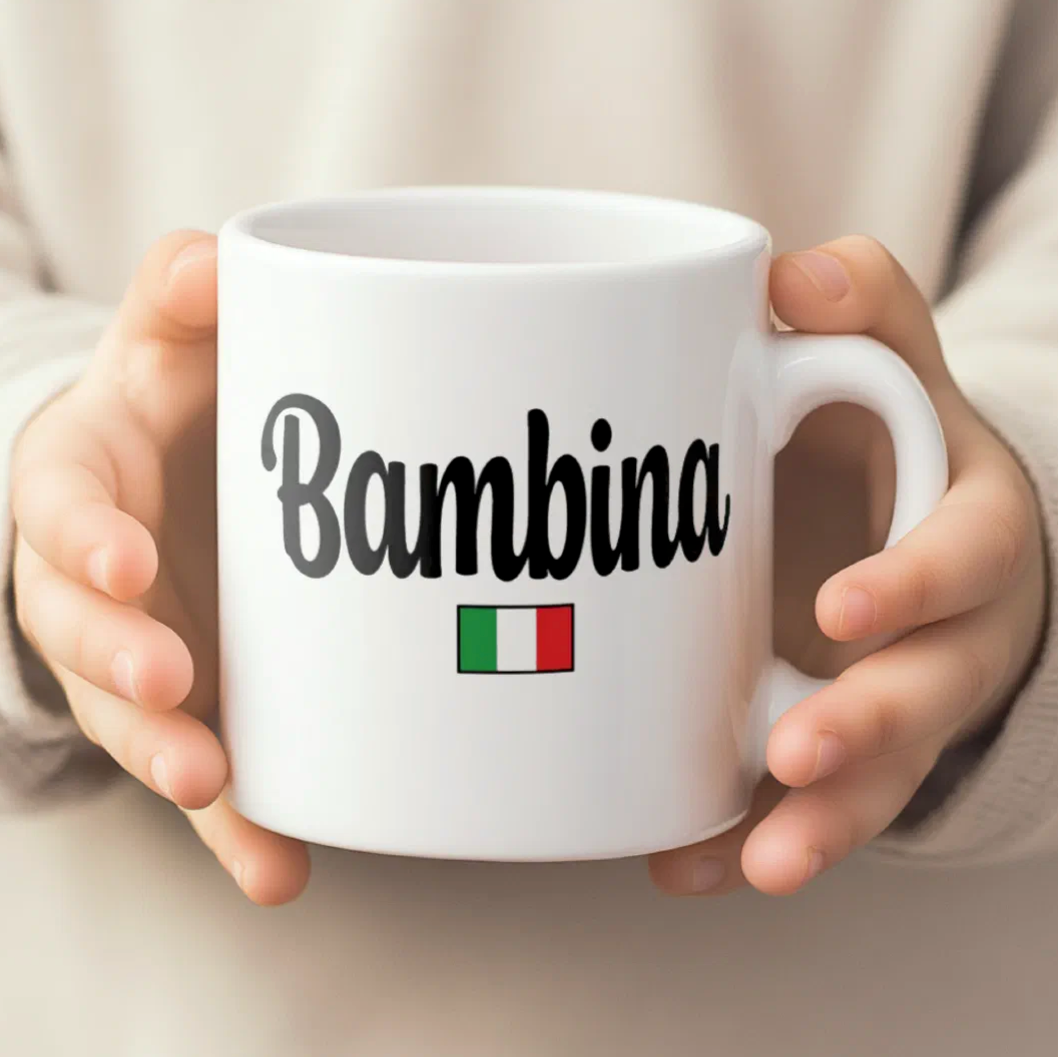 White mug with 'Bambina' and Italian flag held by hands against a neutral background
