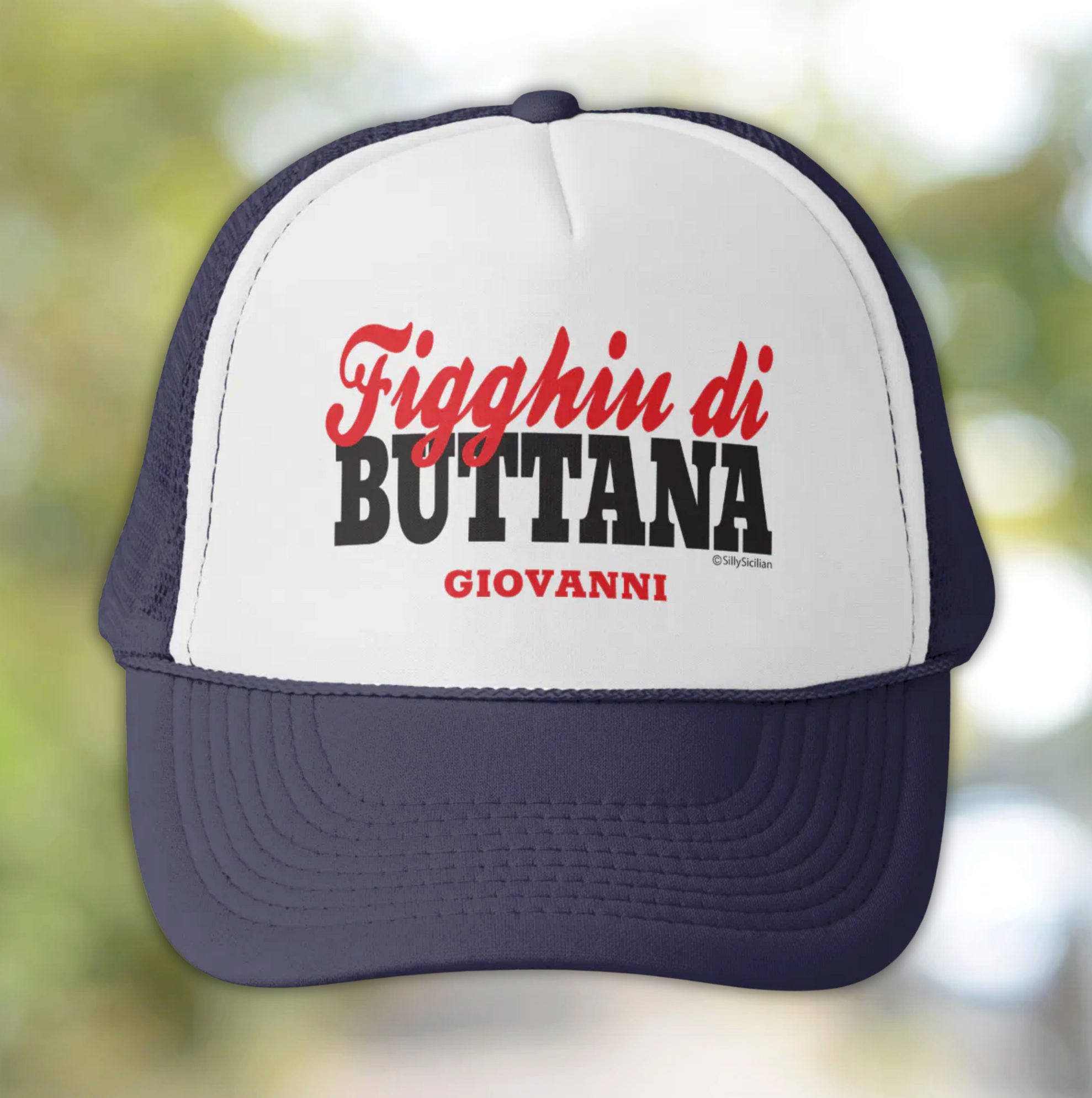 Trucker hat with text 'Figghiu di Buttana Giovanni' personalized text on a blurred natural background