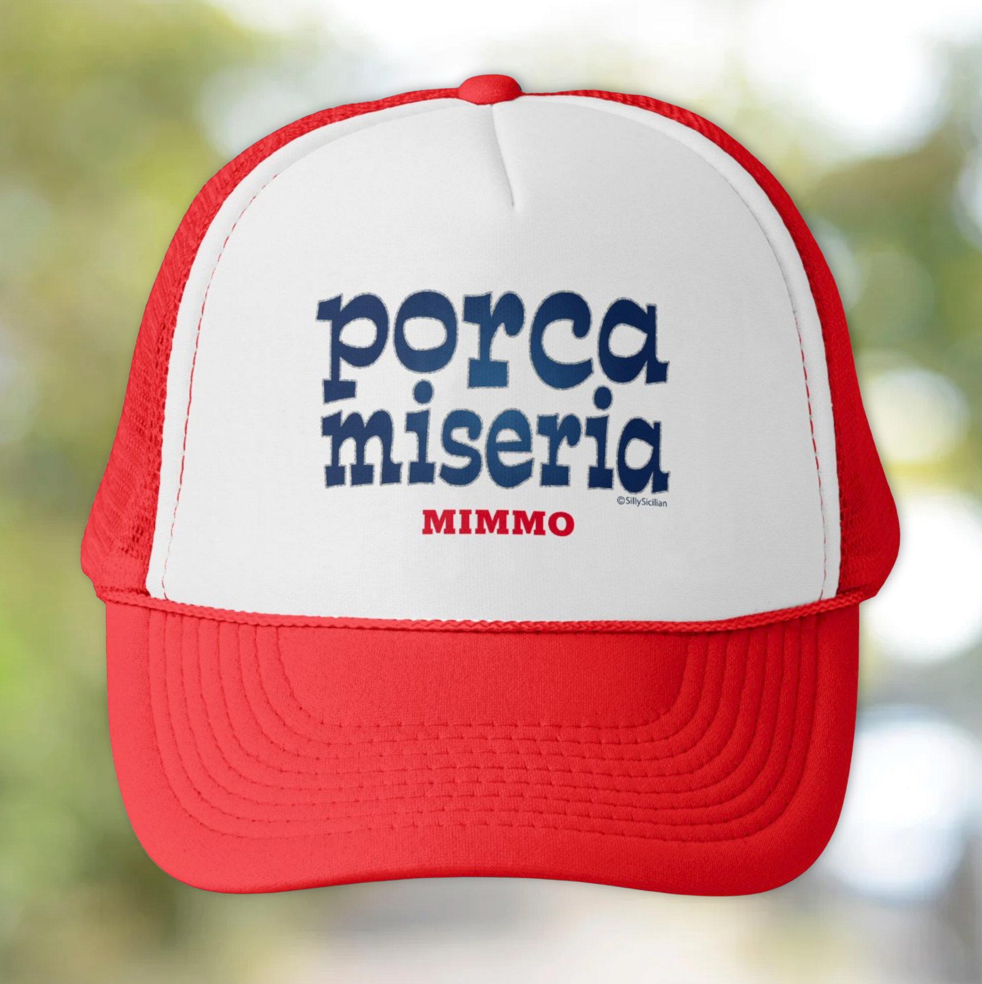 Red and white cap with blue text 'porca miseria' and red 'MIMMO' personalized on a blurred natural background.