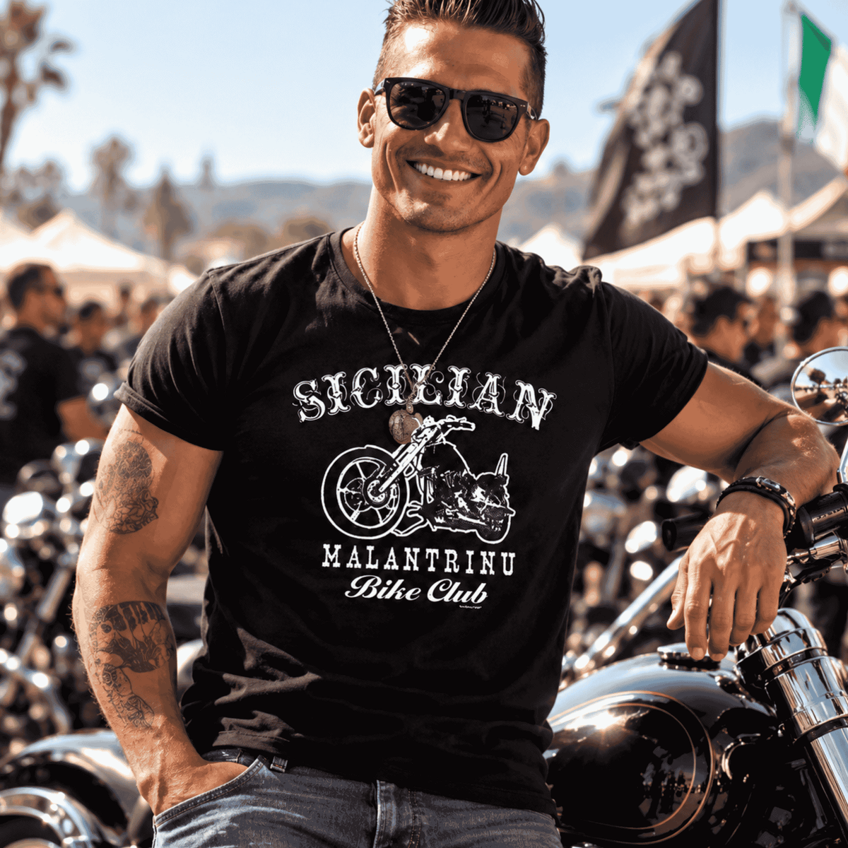 Man wearing a black Sicilian Malantrinu Bike Club T-shirt featuring vintage chopper artwork and bold tattoo-style lettering, posing beside a motorcycle at a biker rally. An edgy, humorous Sicilian heritage gift for motorcycle enthusiasts and riders who love old-school outlaw style.
