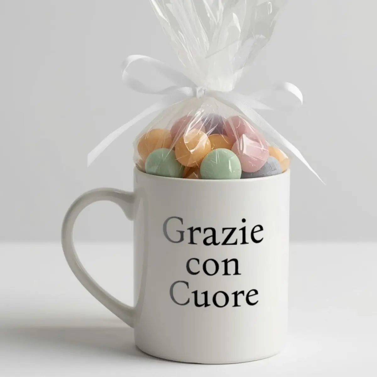 Grazie con cuore (thank you with heart) minimalist black serif font on white mug with cellophane and candies tied with white satin bow. Italian and Sicilian heritage keepsake favor, baby shower favor idea, wedding shower favor idea, bridal shower favor, Italian party favor, Italian wedding favor, gift for guests, Italian celebration favor.
