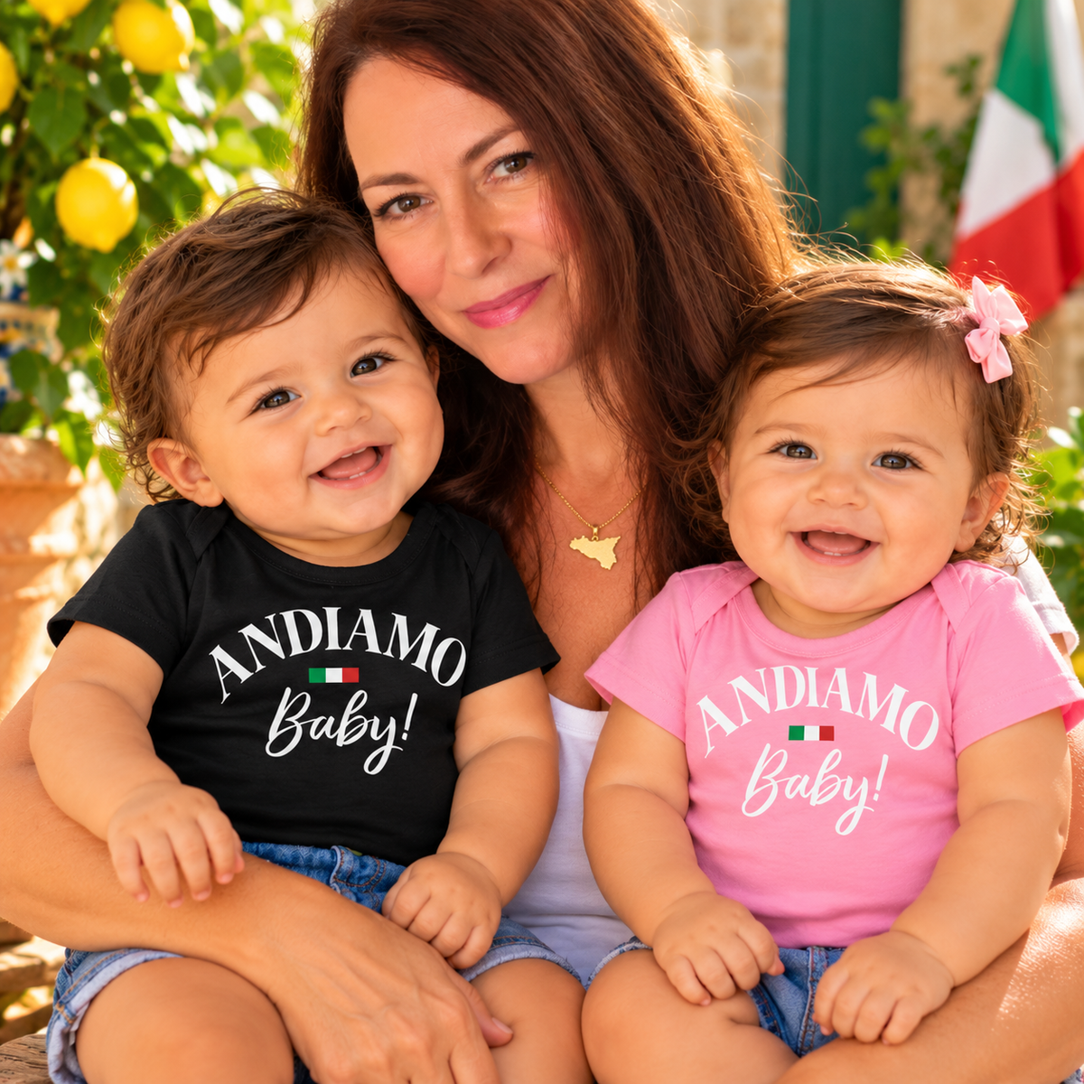 Smiling Italian babies wearing black and pink “Andiamo Baby!” T-shirts with Italian flag accents, lovingly held by Leandra.