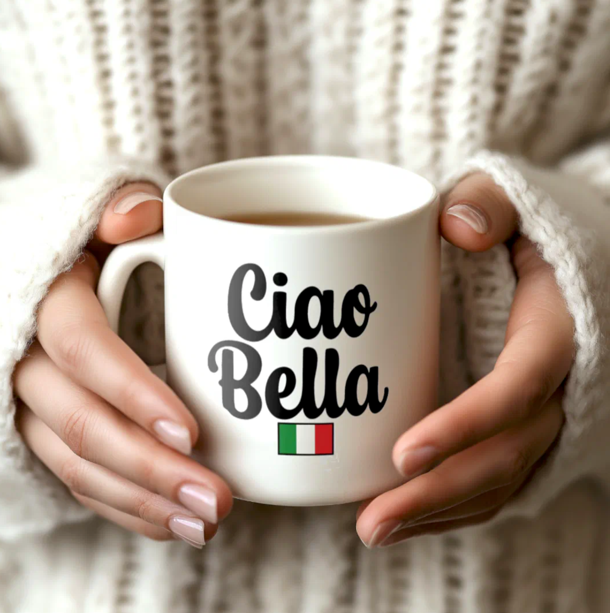 White mug with 'Ciao Bella' text held by hands against a textured beige background