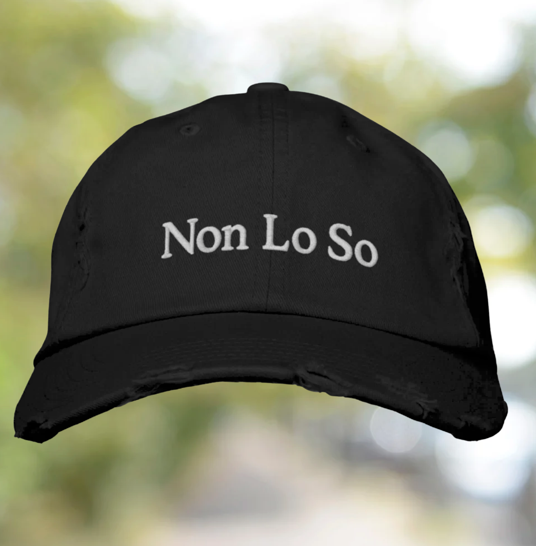 Black cap with 'Non Lo So' text on a blurred natural background