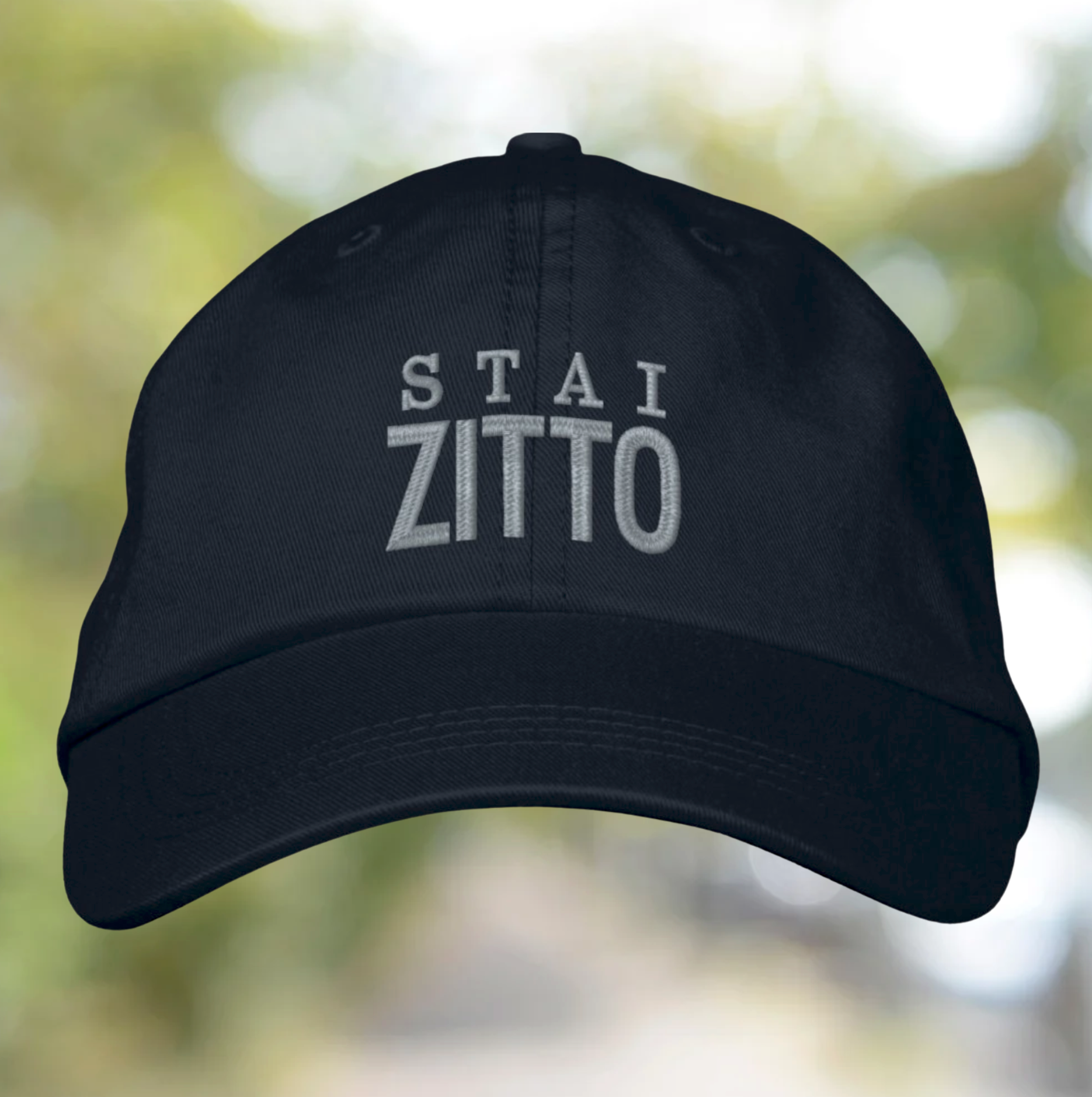 Black cap with 'STAI ZITTO' text on a blurred natural background