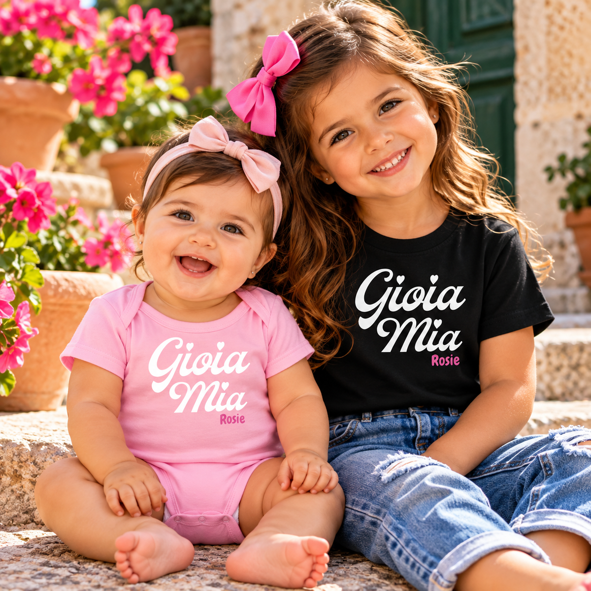 Two sisters wearing personalized Gioia Mia Italian baby bodysuit and girls' T-shirt in pink and black.