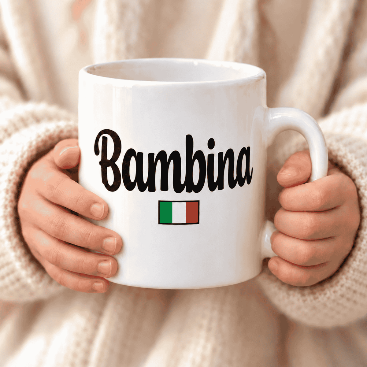 White mug with 'Bambina' and Italian flag held by hands against a neutral background