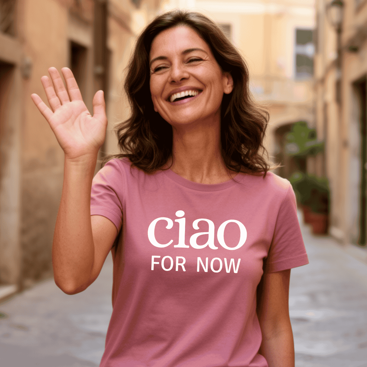 Woman wearing a pink t-shirt with 'ciao FOR NOW' text, waving happily; Italian heritage travel lovers gift