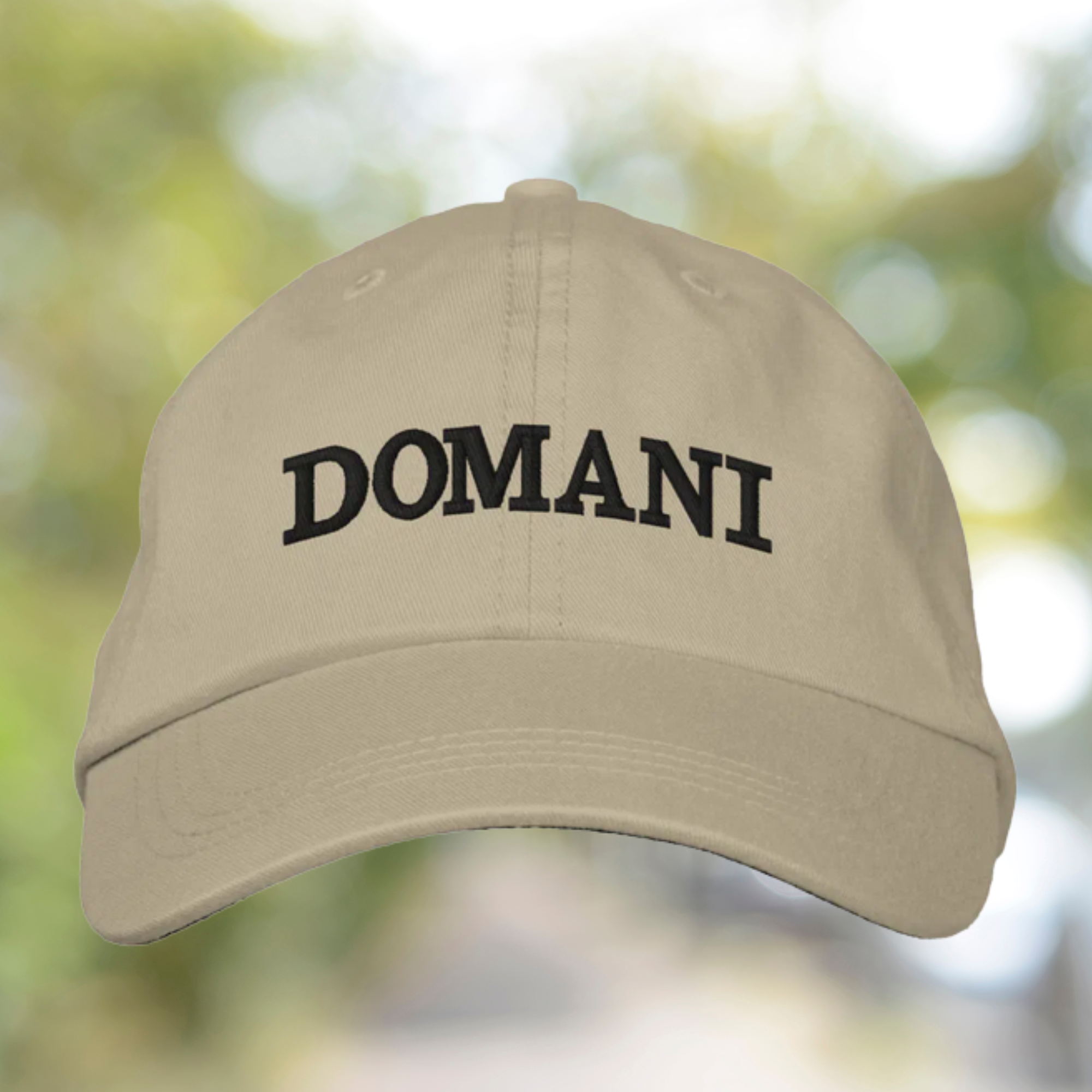 Beige cap with 'DOMANI' text on a blurred natural background