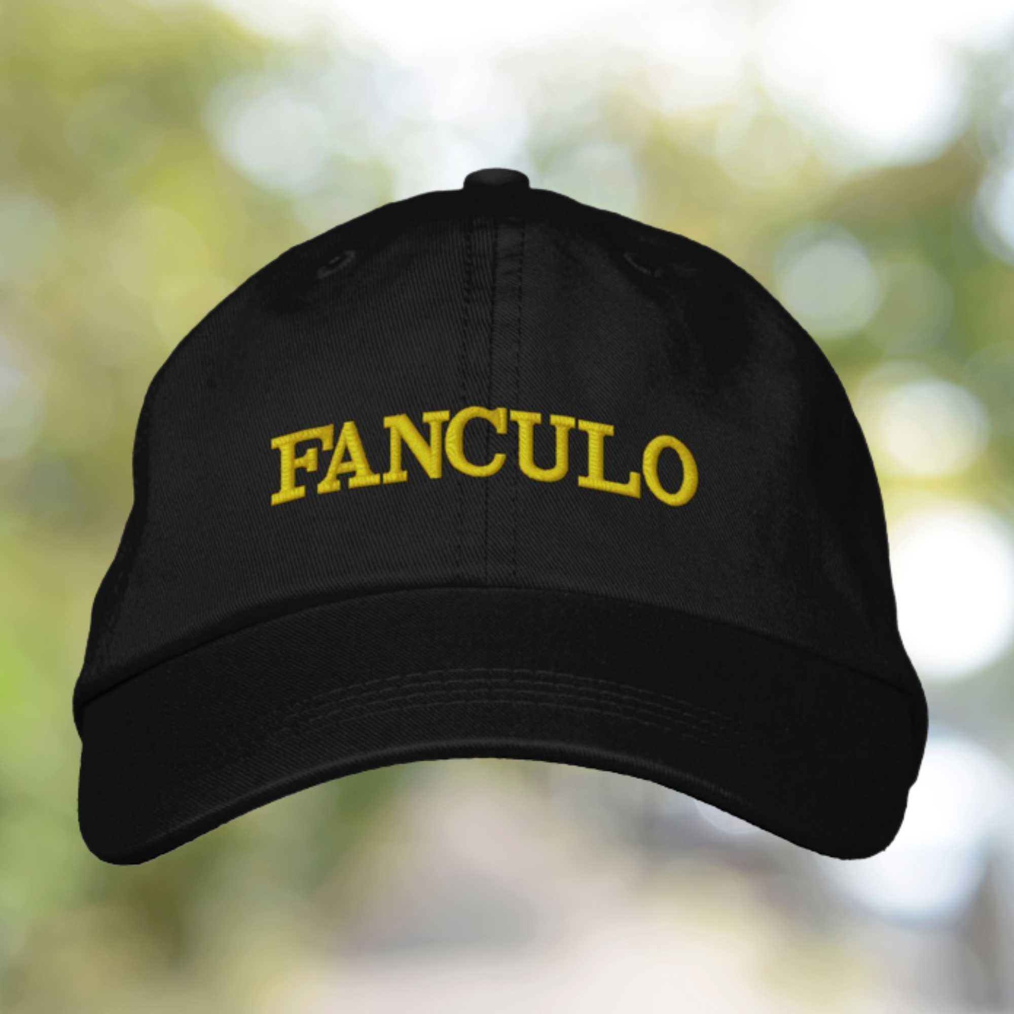 Black cap with 'FANCULO' in yellow on a blurred natural background