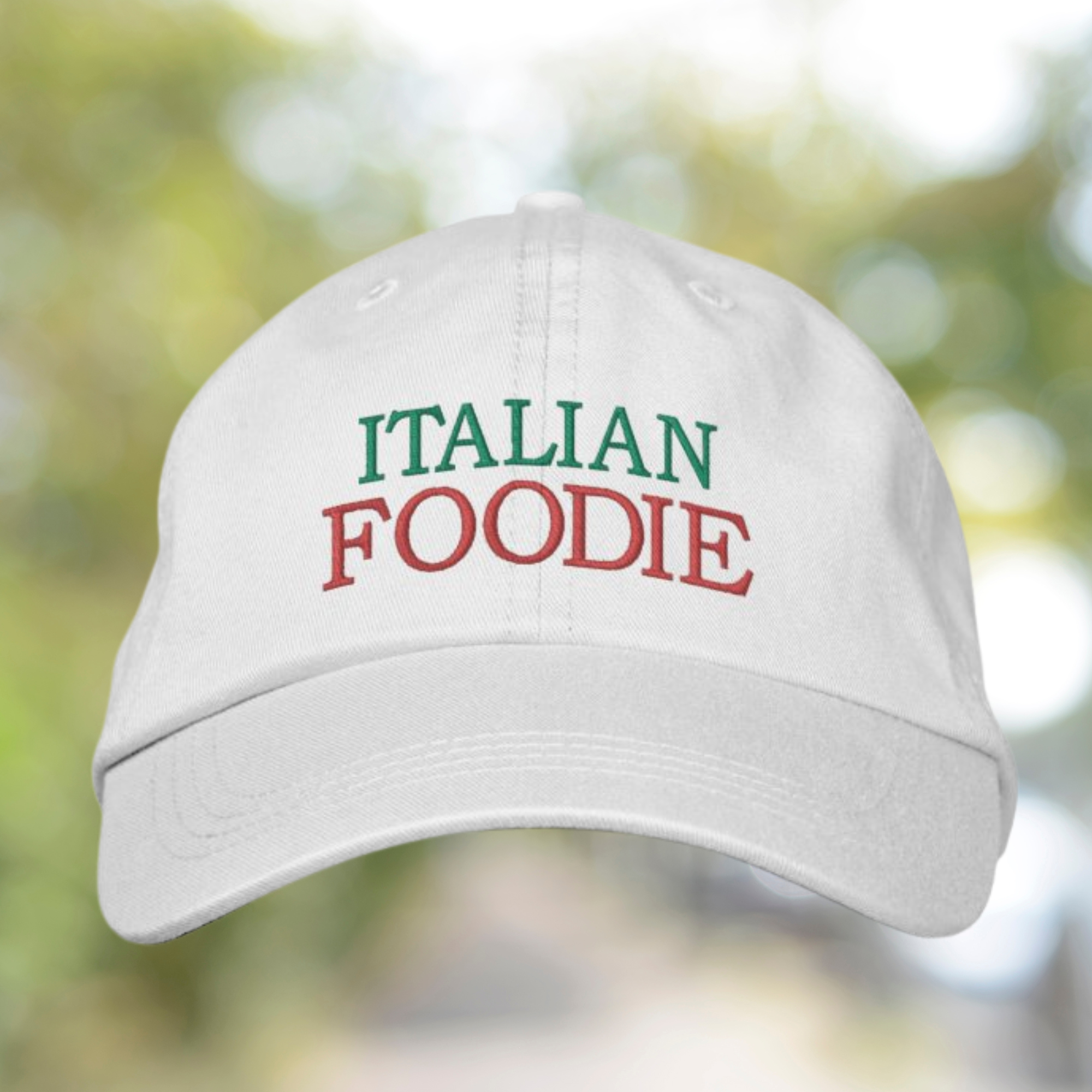 White cap with 'ITALIAN FOODIE' text in green and red on a blurred natural background