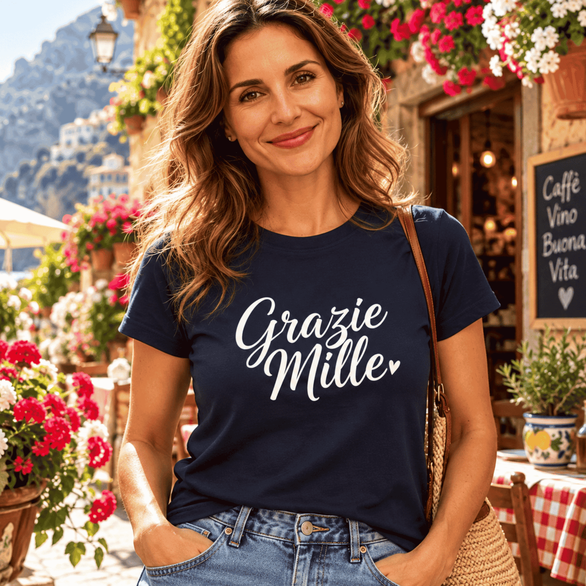 Woman wearing a navy Grazie Mille T-shirt at a sunny Italian café surrounded by colorful flowers.