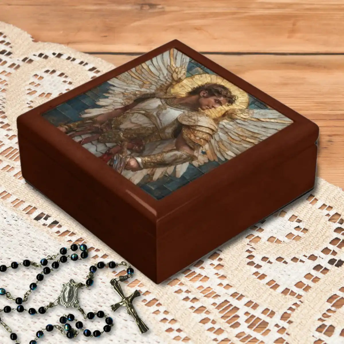 Wooden keepsake box with an Archangel Michael design on a lace tablecloth with a rosary beside it