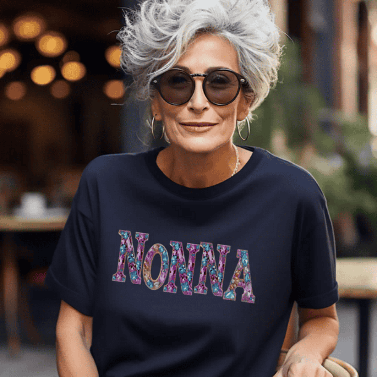 Woman wearing a navy blue t-shirt with 'NONNA' printed in colorful letters printed faux gems jewels - Italian heritage gift