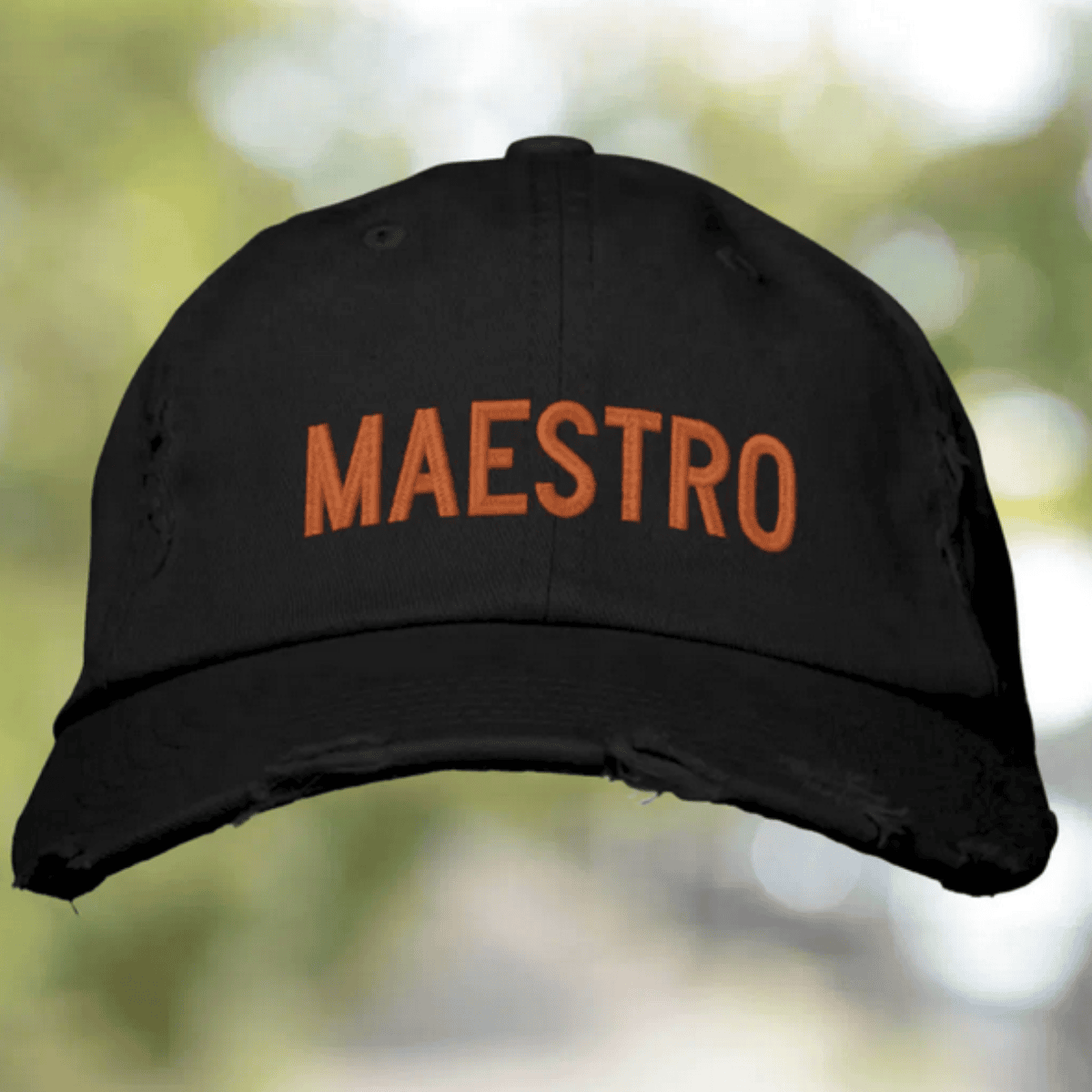 Black cap with 'MAESTRO' in orange on a blurred natural background